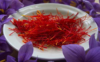 Bord gevuld met saffraandraden en omgeven door saffraanbloemen.
